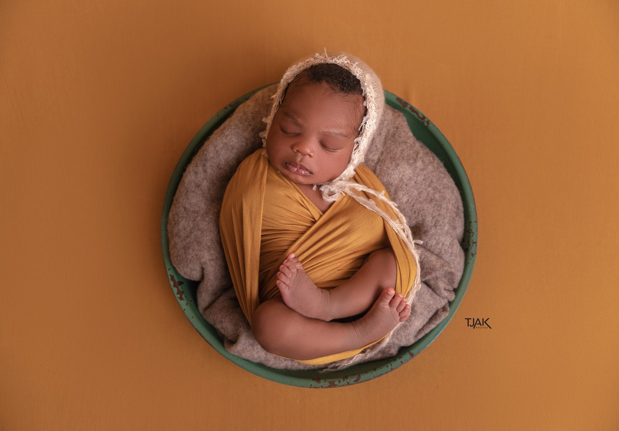 Baby photoshoot of a newborn wearing bonnet in a bowl by a maternity photographer