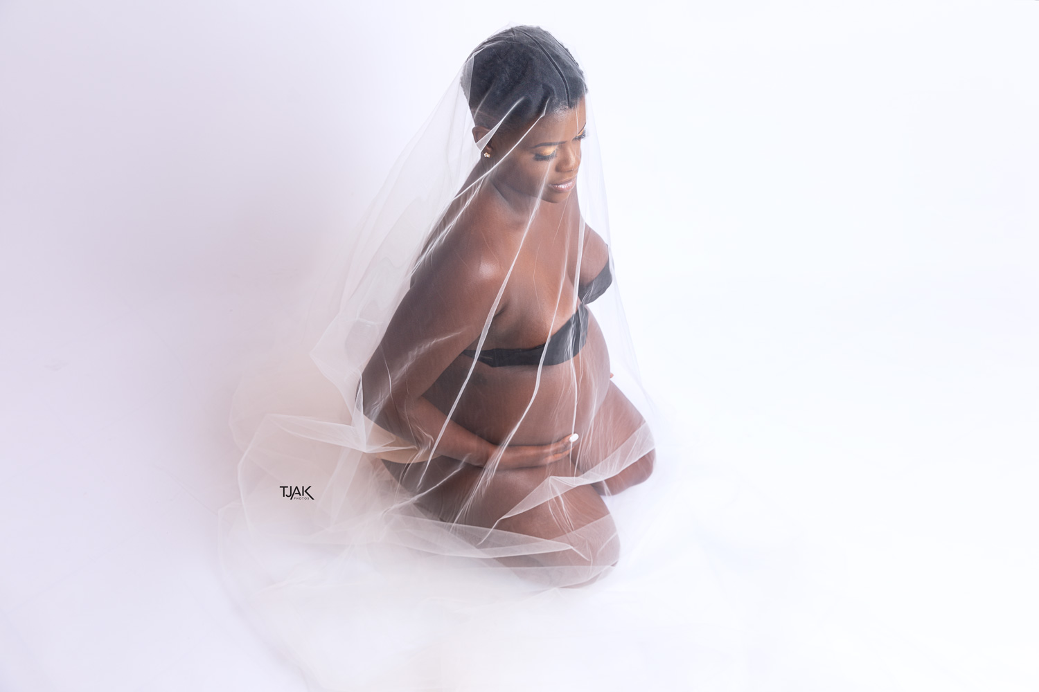 Fine art maternity photography of a pregnant woman covered with tule fabric in a photography studio in Laurel Maryland