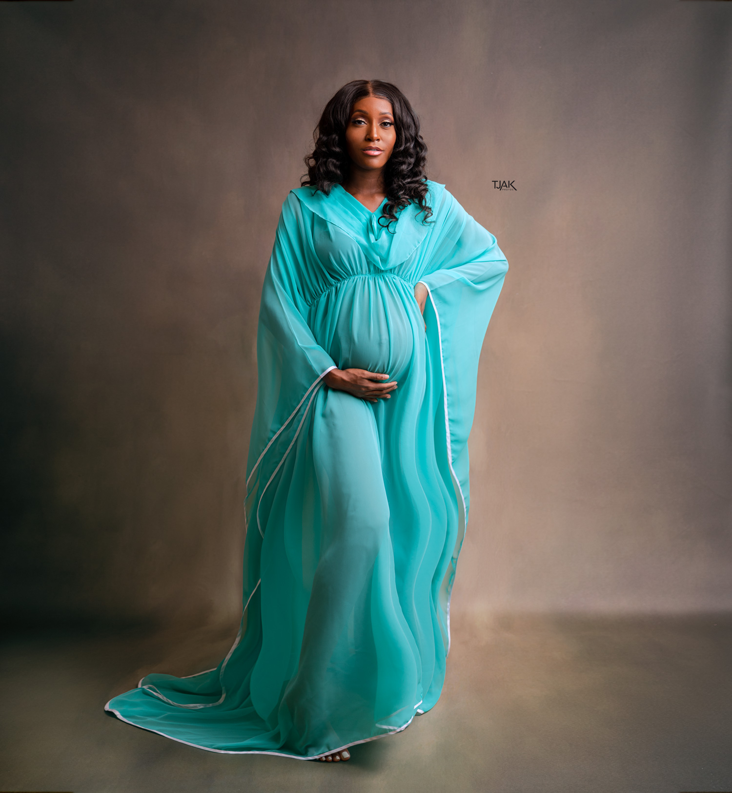 Maternity photoshoot of a woman in a turquoise see through pregnancy dress in a studio in Laurel MD near Savage in Howard County Maryland