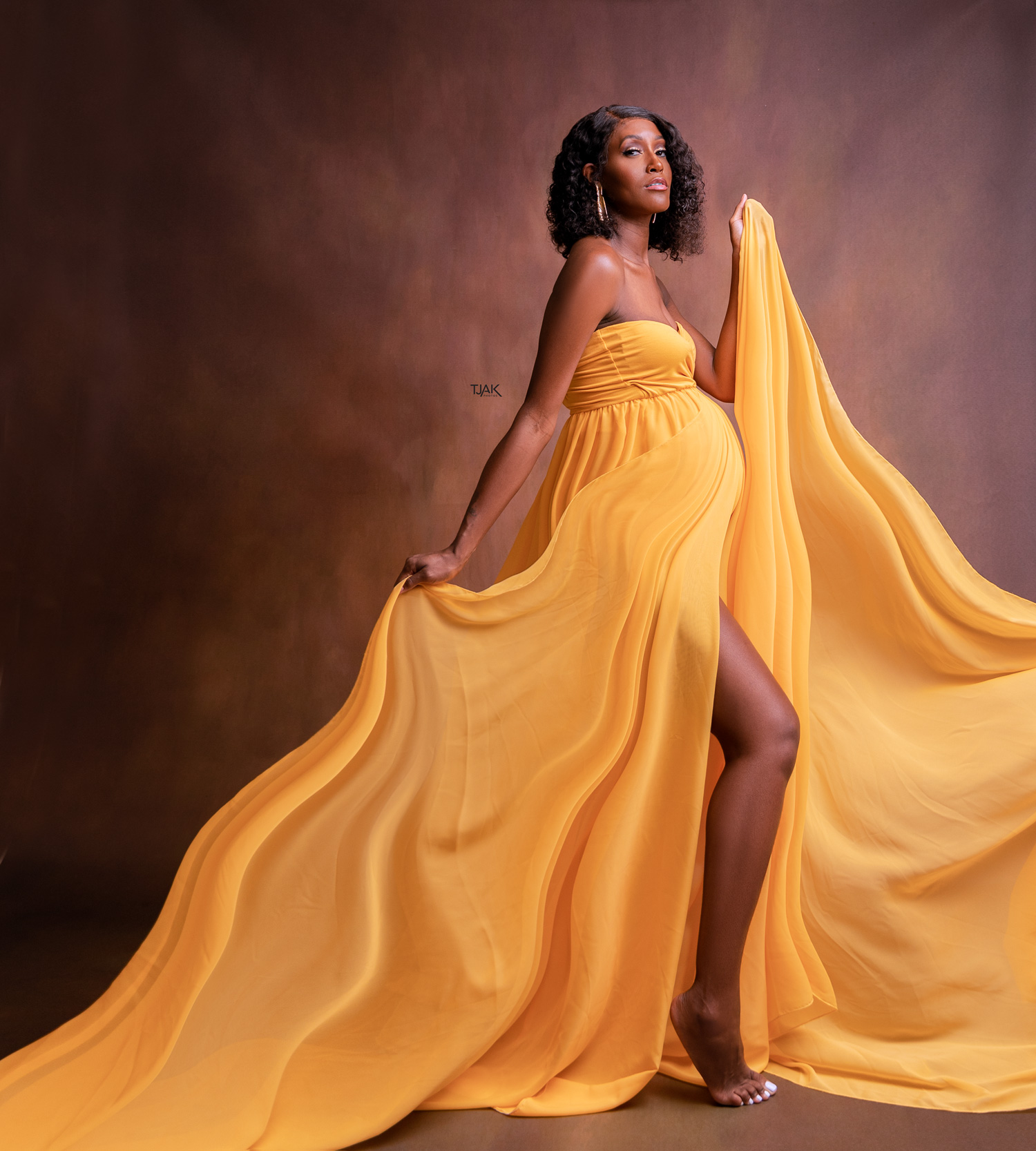 studio maternity photograph of a pregnant woman wearing a yellow body suit with a long fabric by miiestilo in a studio in Laurel MD in Howard County Maryland
