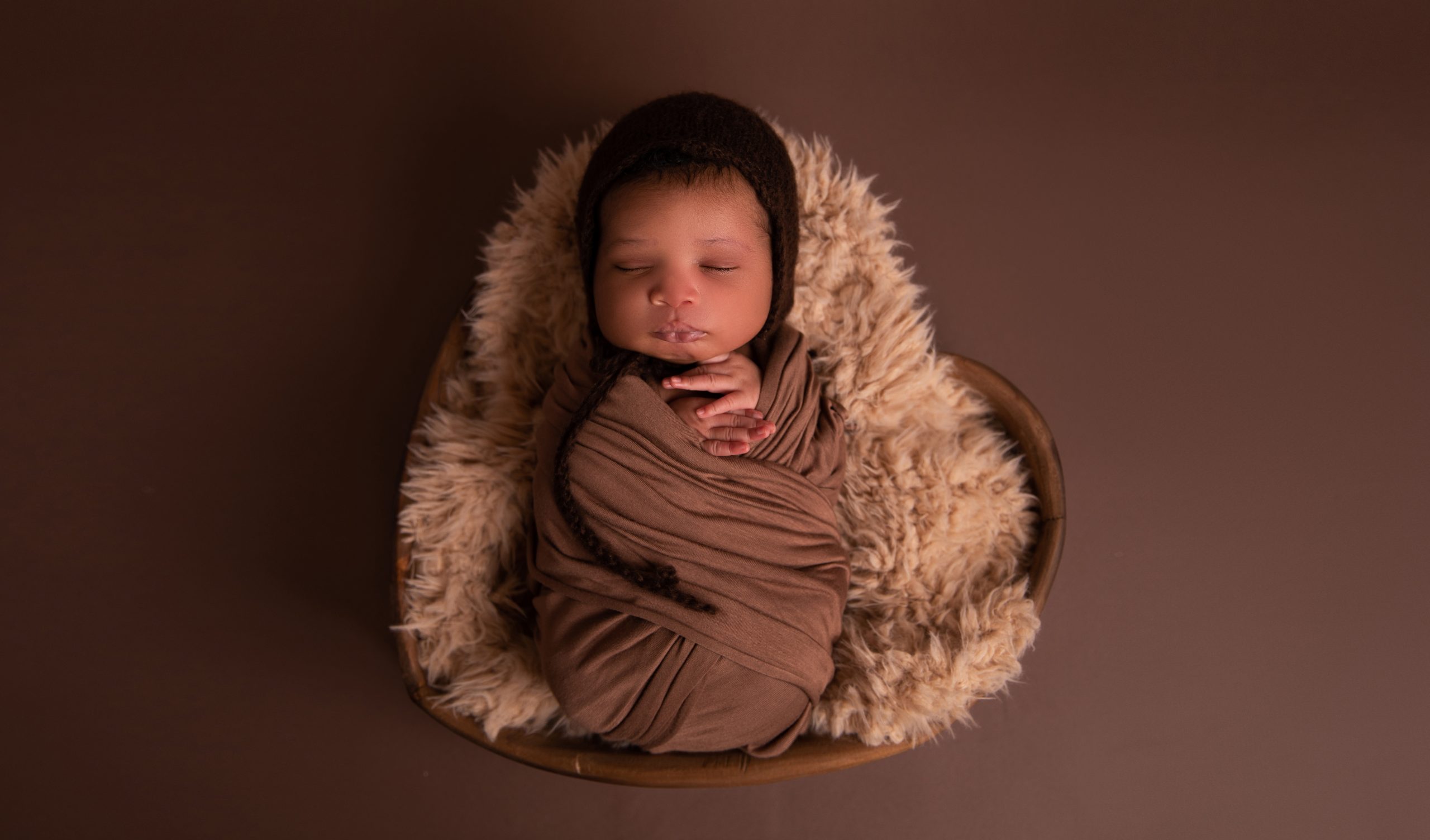newborn photography of a baby wrapped in a brown cloth in a props in a studio in Howard Country Maryland