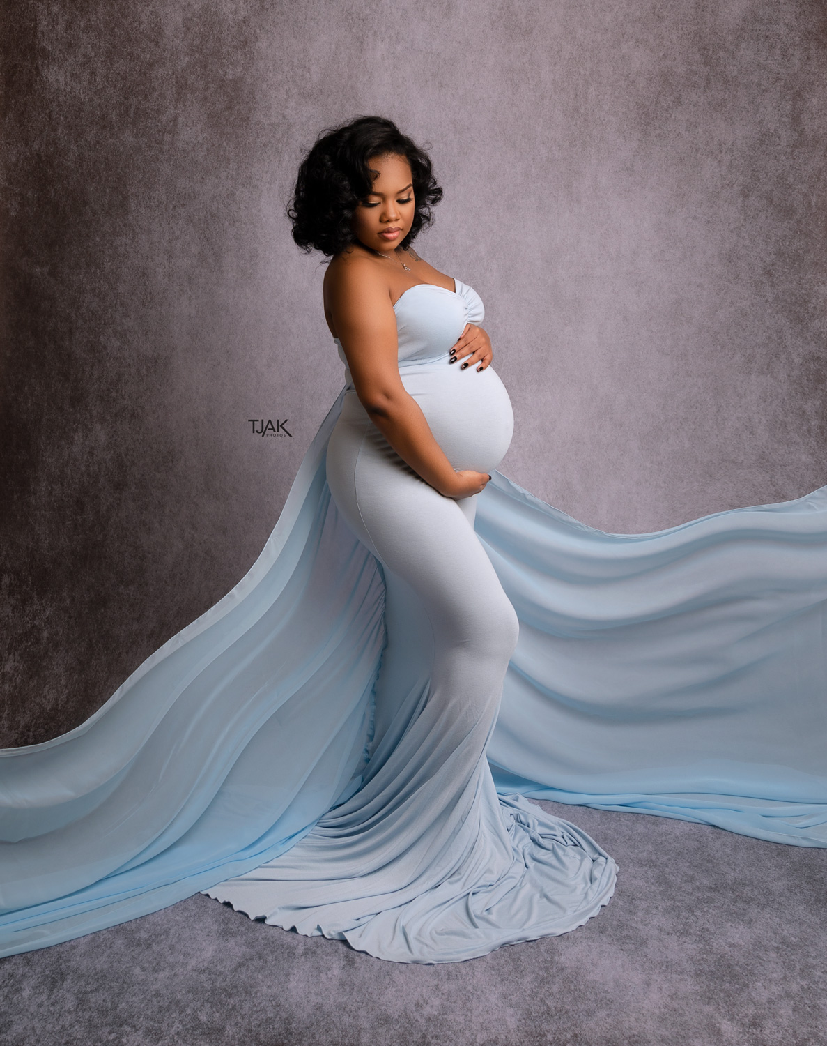 Maternity photograph of a black pregnant woman wearing a blue off-shoulder maternity dress with a long train in a studio near Savage Mill